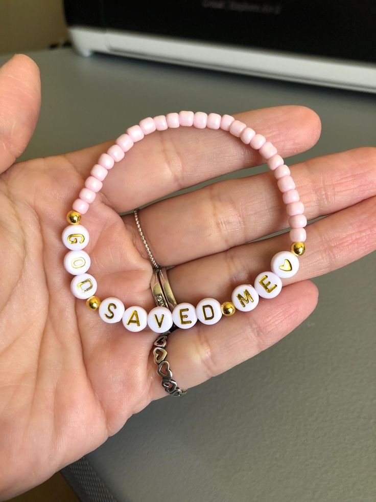 a person holding a pink beaded bracelet with the word love spelled in small letters