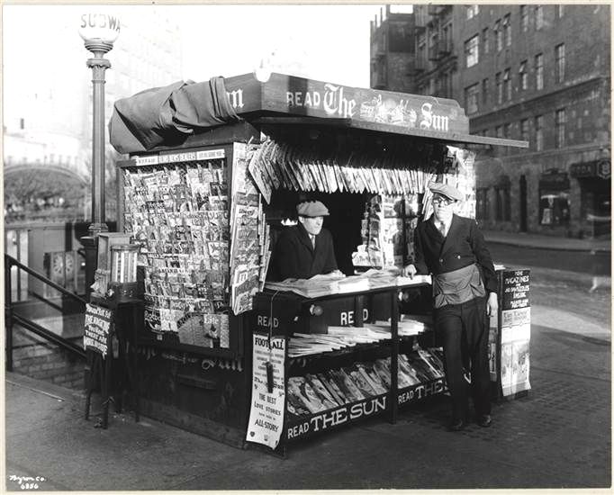 two men standing in front of a newspaper stand