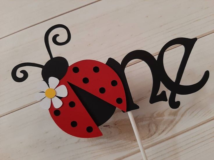 a red and black ladybug cake topper on a white wooden table with the word love spelled out