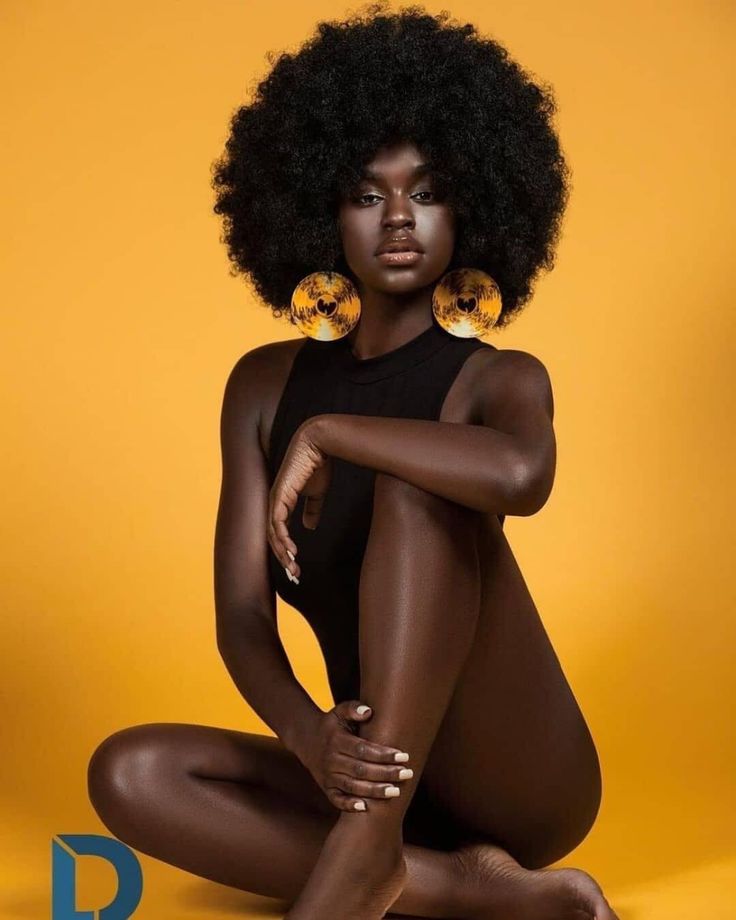 a woman with an afro sitting on the ground wearing gold hoop earrings and black bodysuit