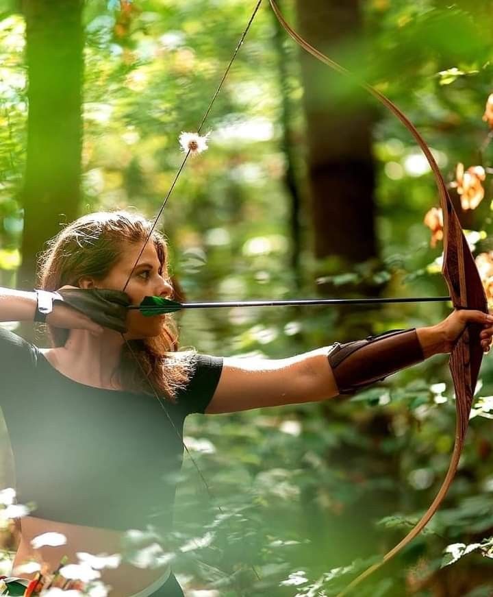 a woman is aiming an arrow in the forest