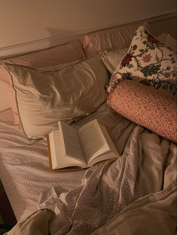 an open book sitting on top of a bed next to pillows