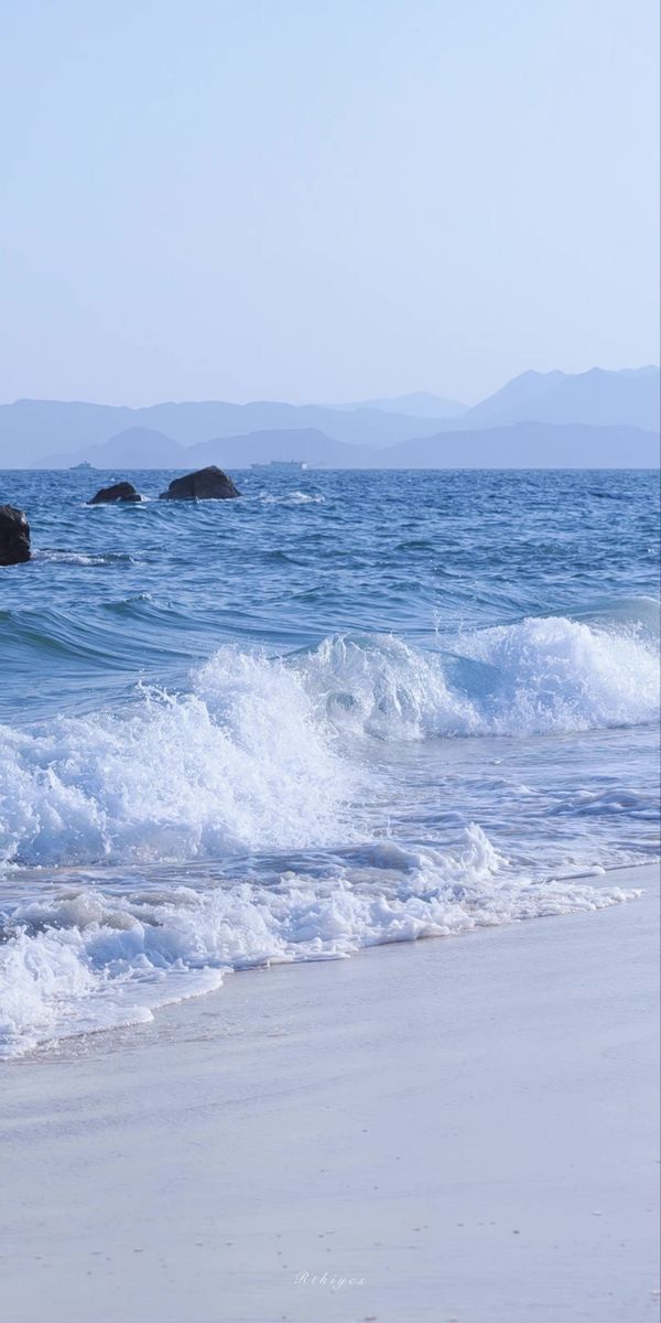 an ocean view with waves crashing on the shore and rocks in the water behind it