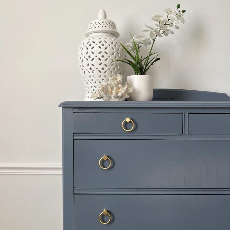 a blue dresser with white flowers on top and a vase sitting on it's side