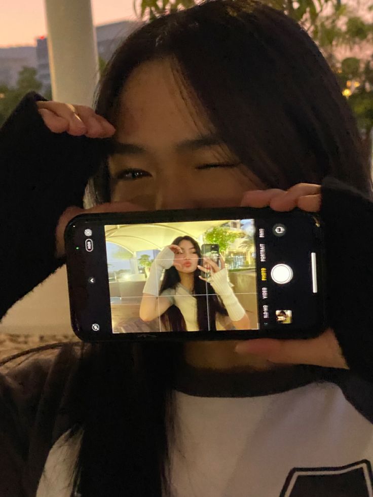 a woman holding up her cell phone to take a selfie in front of her face