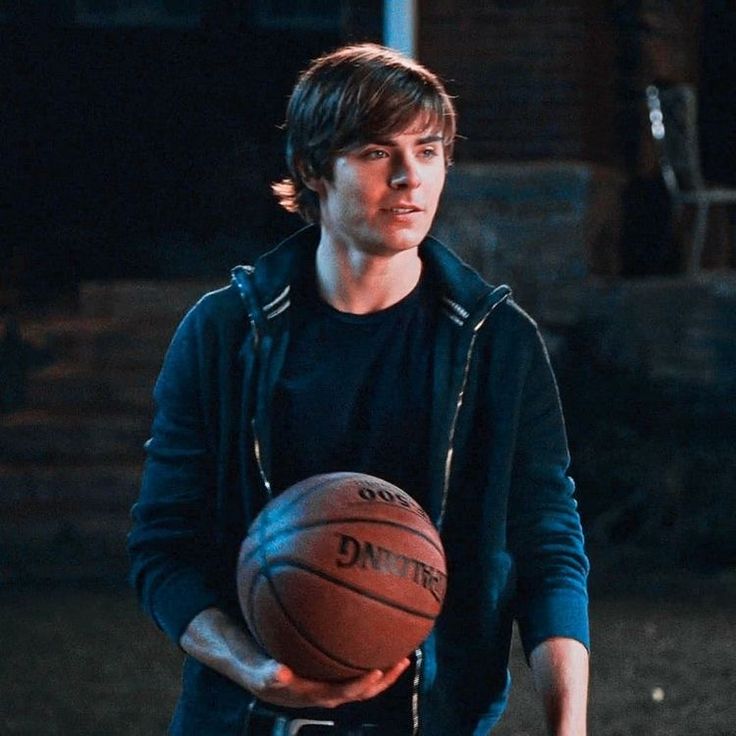 a young man holding a basketball in his right hand and wearing a black hoodie