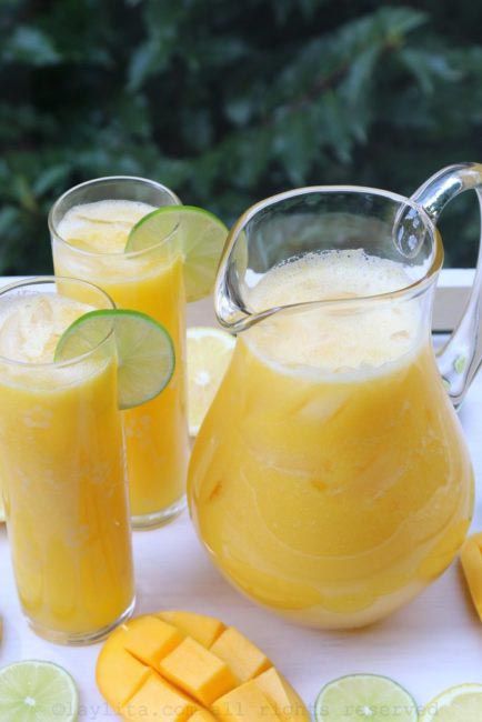 two pitchers of orange juice with sliced mangoes and limes next to them on a tray