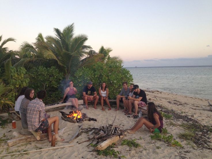 a group of people sitting around a campfire on the beach