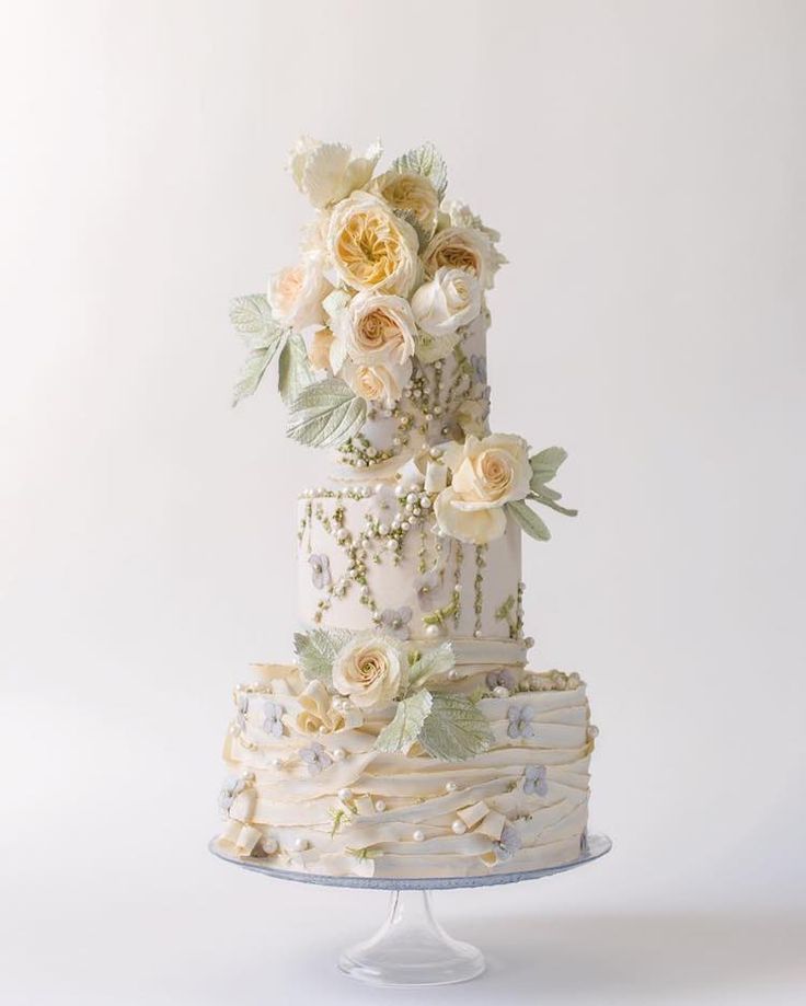 a three tiered cake with white flowers and leaves on the top is shown in front of a white background