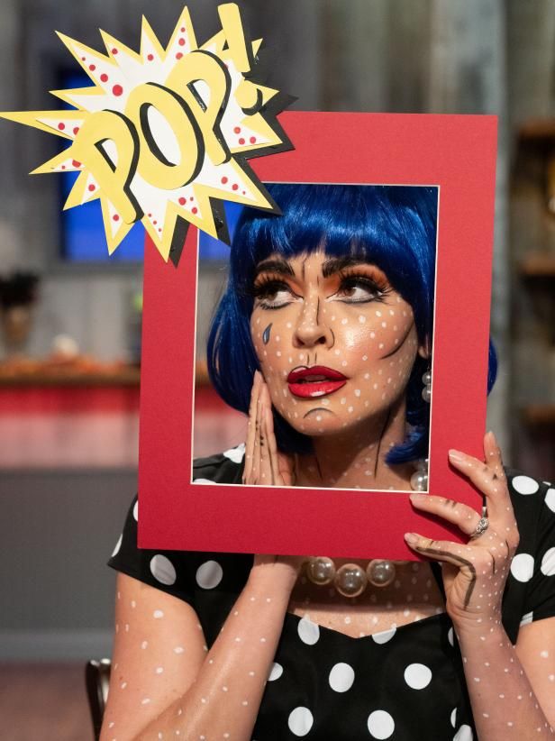 a woman with blue hair and makeup holding up a red frame that has a picture of herself painted on it