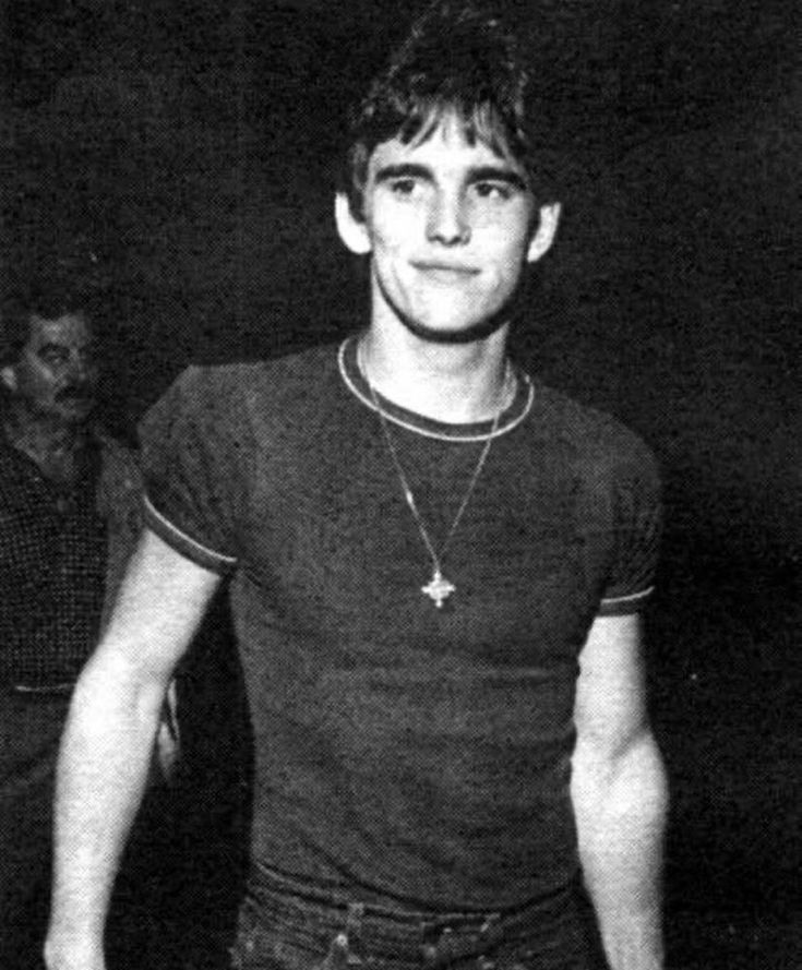 black and white photo of young man in dark room with two men standing behind him