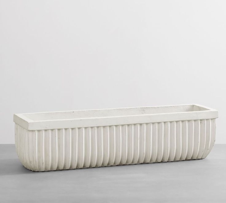 a white rectangular planter sitting on top of a cement floor next to a wall