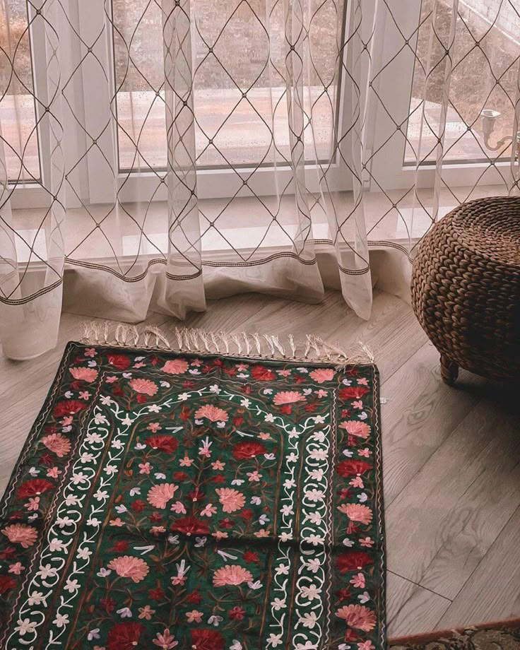 a rug sitting on the floor in front of a window with sheer curtains behind it