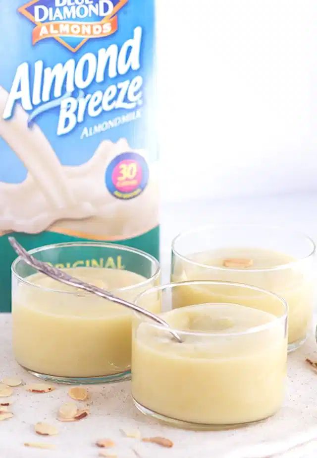 three glasses filled with pudding next to a carton of almond milk