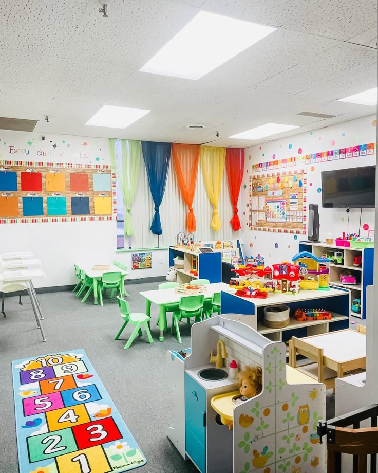 an empty classroom with toys and desks on the floor in front of colorful drapes