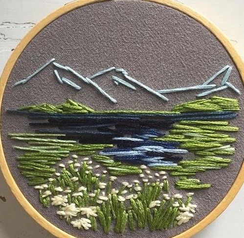 an embroidered wall hanging with flowers and mountains in the background