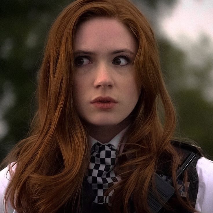 a woman with long red hair wearing a black and white checkered tie, looking at the camera