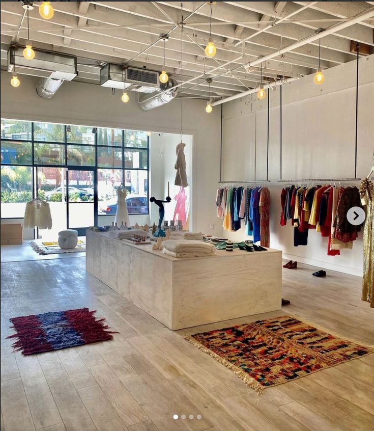 the inside of a clothing store with lots of clothes hanging on racks and rugs