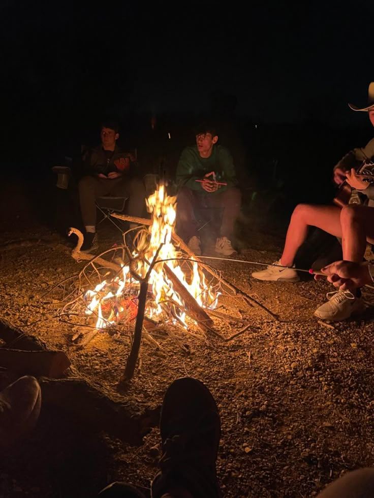 people sitting around a campfire at night with their cell phones in the fire pit