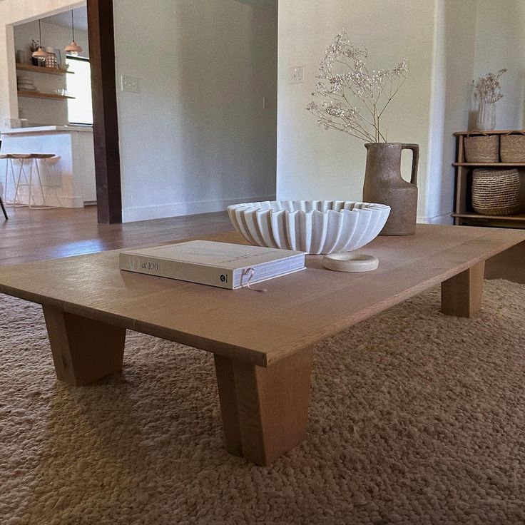 a living room with a coffee table, vase and books on the carpeted floor