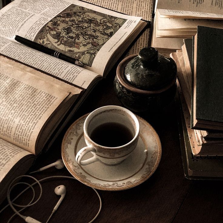 an open book, cup of coffee and headphones on a table with other books