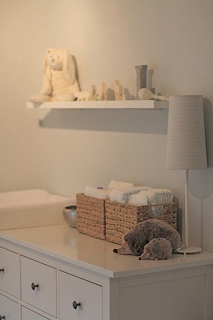 a baby crib in a white nursery with stuffed animals on the dresser and shelves