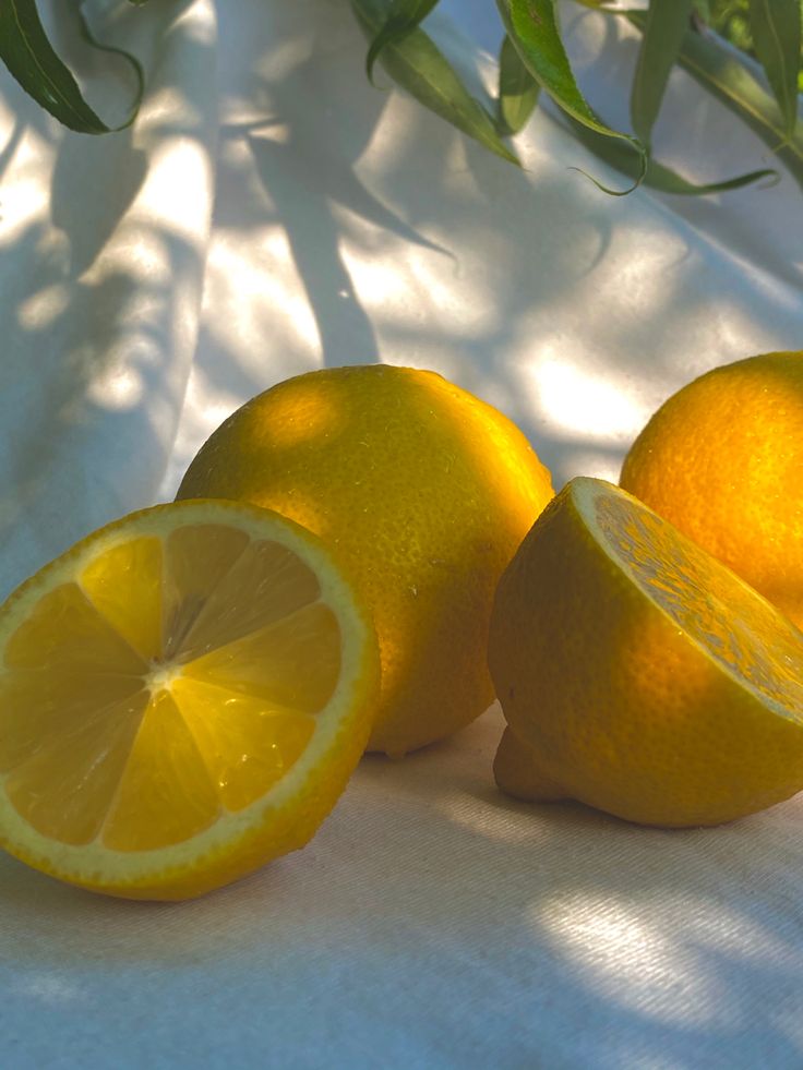 two lemons sitting next to each other on a white surface with green leaves in the background