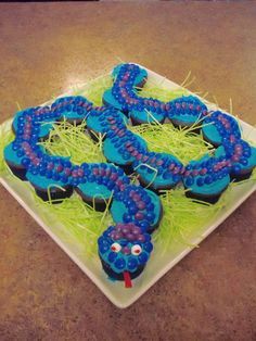 blue and purple cupcakes on a square plate with grass in the shape of a snake