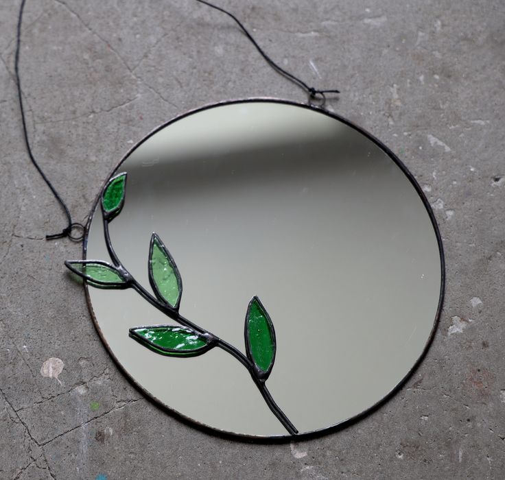 a round mirror with a green leaf on it sitting on the ground next to a string