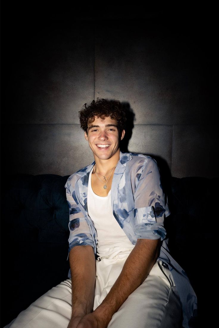 a young man sitting on top of a couch in front of a black wall smiling at the camera