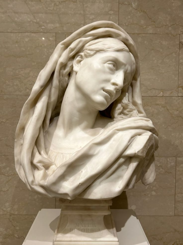 a marble bust of a woman with a scarf around her head in front of a wall