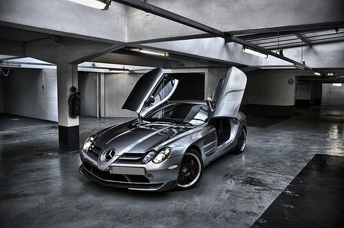 a silver sports car parked in a parking garage with its doors open and the hood up