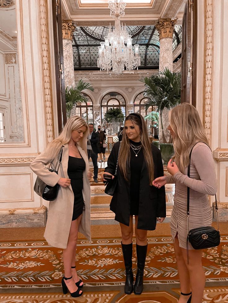 three beautiful young women standing next to each other in front of a chandelier