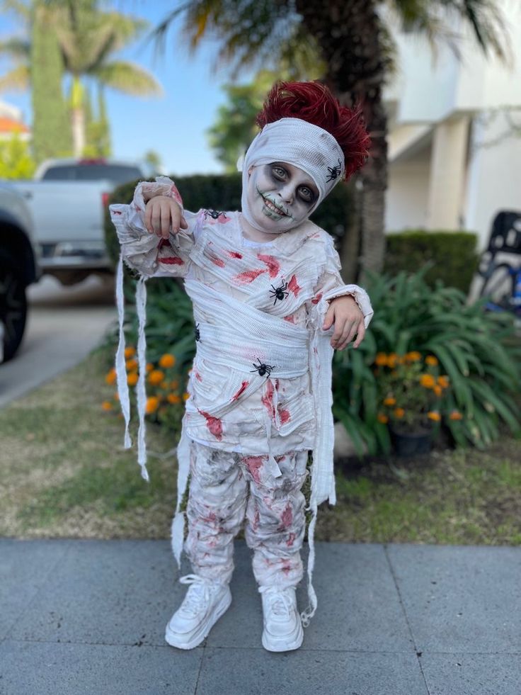 a young child dressed as a skeleton with red hair and makeup, standing on the sidewalk