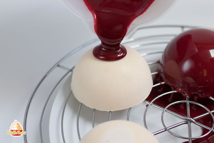 an egg is being poured on top of two eggs in a metal rack with red sauce