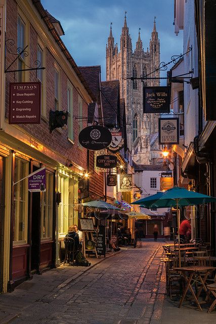 an alleyway with tables and umbrellas in front of the cathedral at dusk,