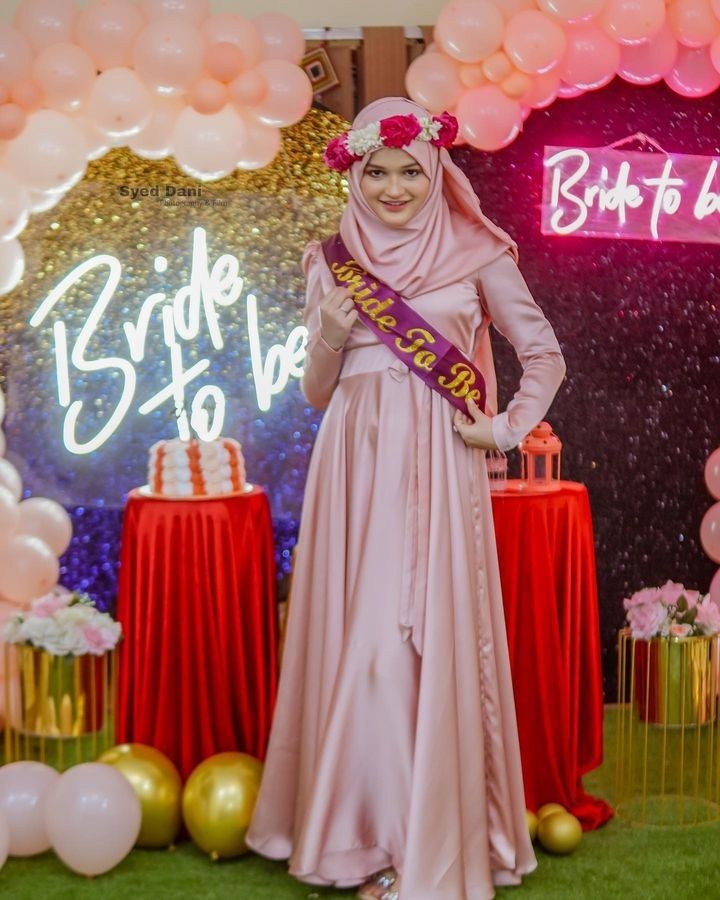 a woman in a hijab is standing next to balloons and presents on the stage