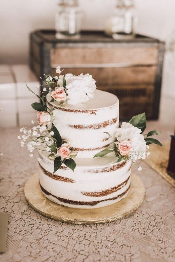 a three tiered cake with flowers and greenery sits on top of a table