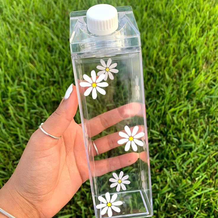 a hand holding a clear water bottle with white flowers painted on the front and sides