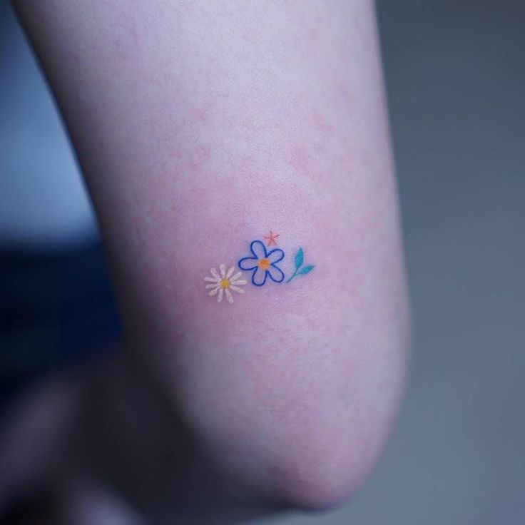 a small flower tattoo on the left side of the leg, with blue and yellow flowers