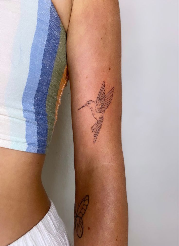 a woman's arm with a tattoo on it and a hummingbird in flight