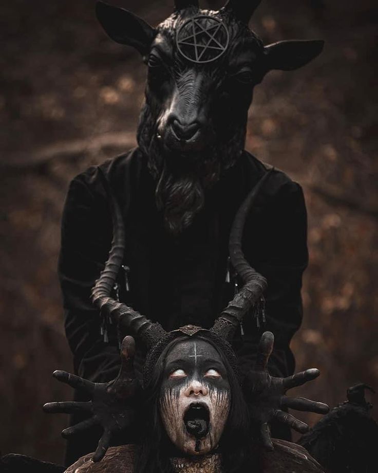 a woman with horns on her head sitting next to a goat in front of her