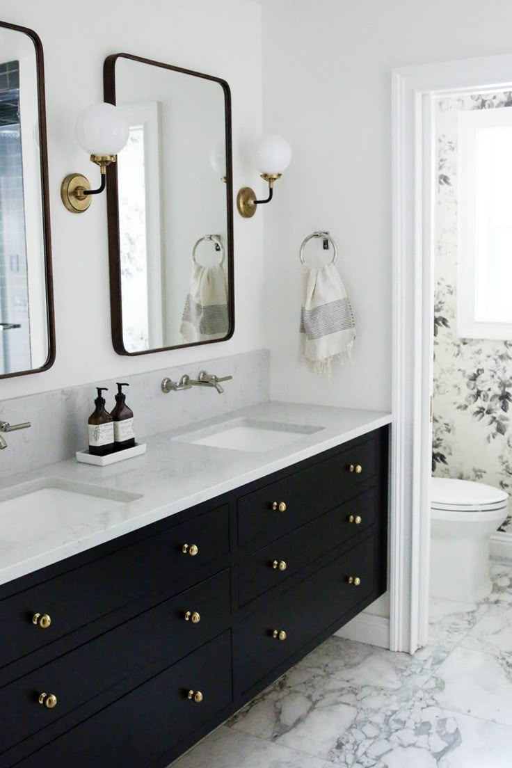 a white and black bathroom with marble counter tops, double sinks, and two mirrors