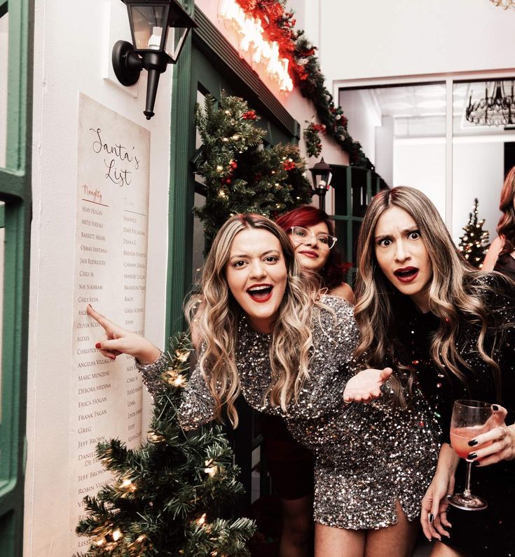 three women standing next to each other in front of a christmas tree with lights on it