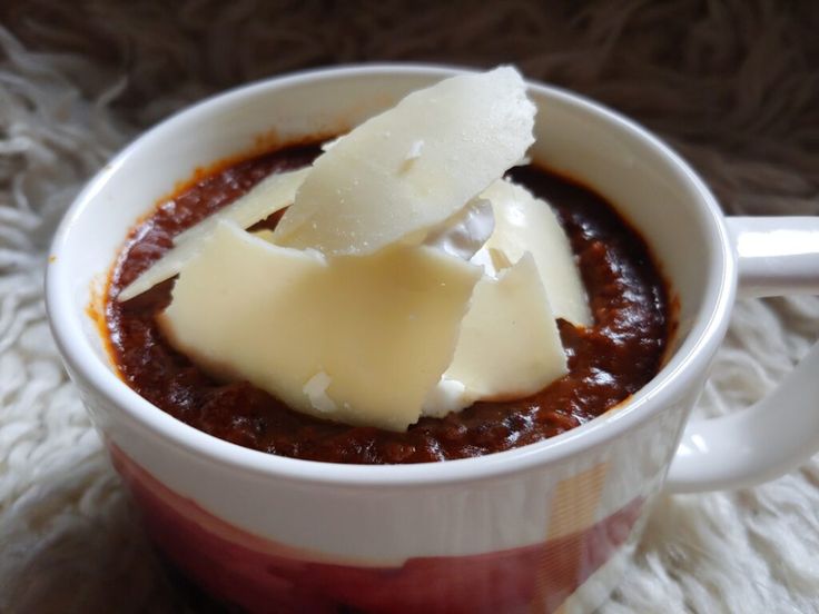 a cup filled with chili and cheese sitting on top of a white tablecloth covered floor