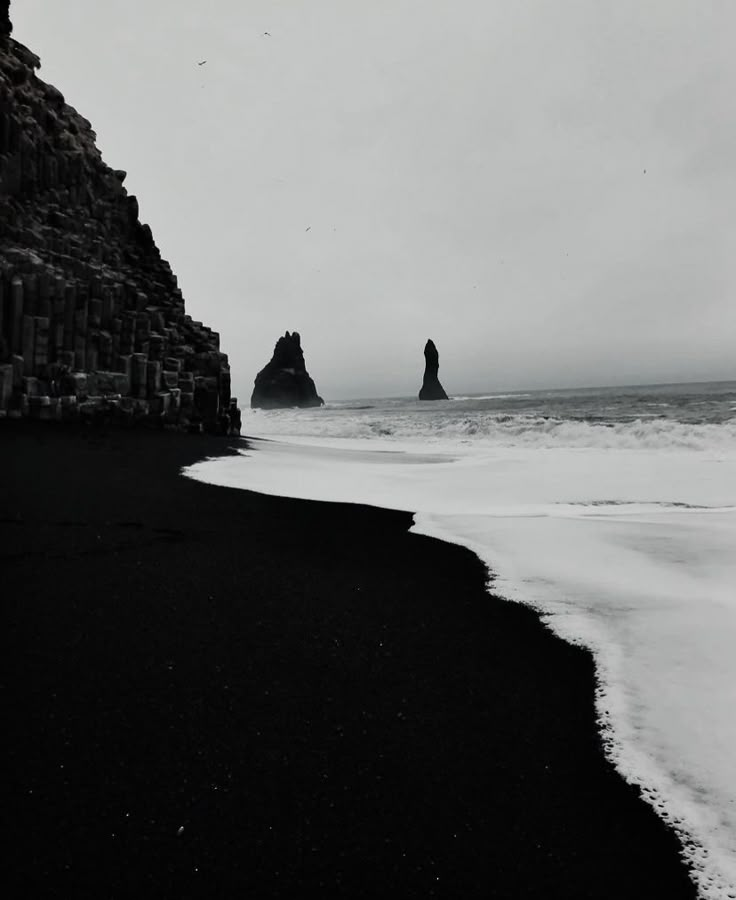 black sand beach with waves coming in to shore and two large rocks sticking out of the water