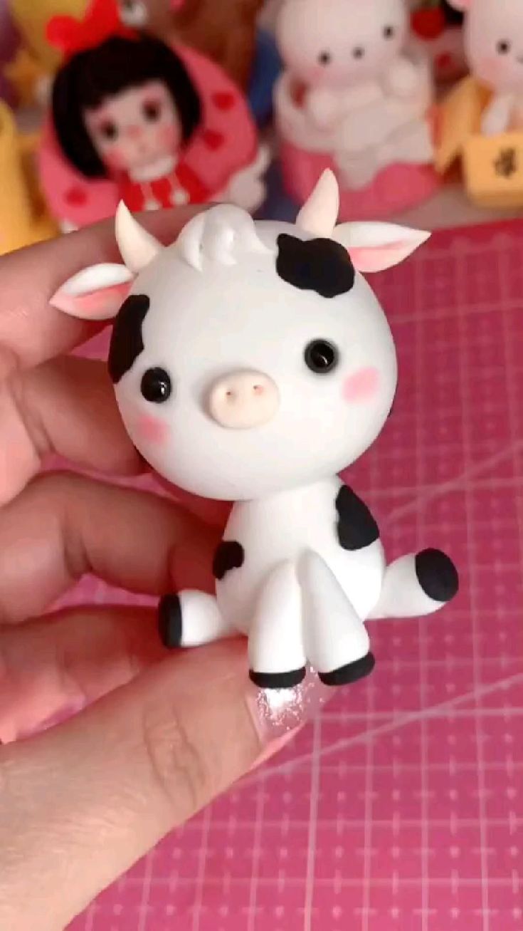 a hand holding a small toy cow on top of a pink table next to other toys