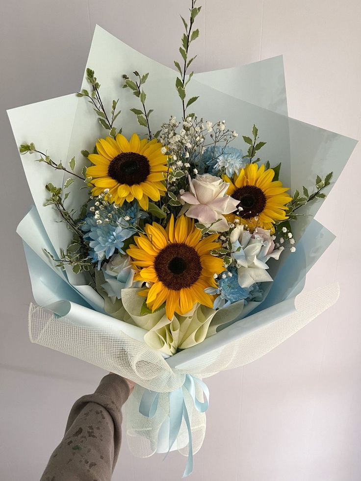 a bouquet of sunflowers and baby's breath is held by a hand