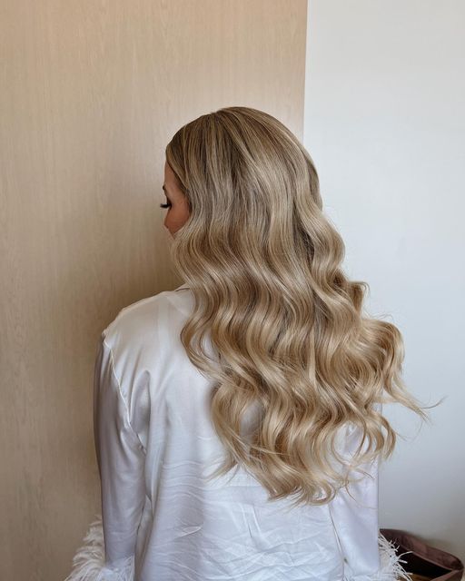 a woman with long blonde hair standing in front of a wall