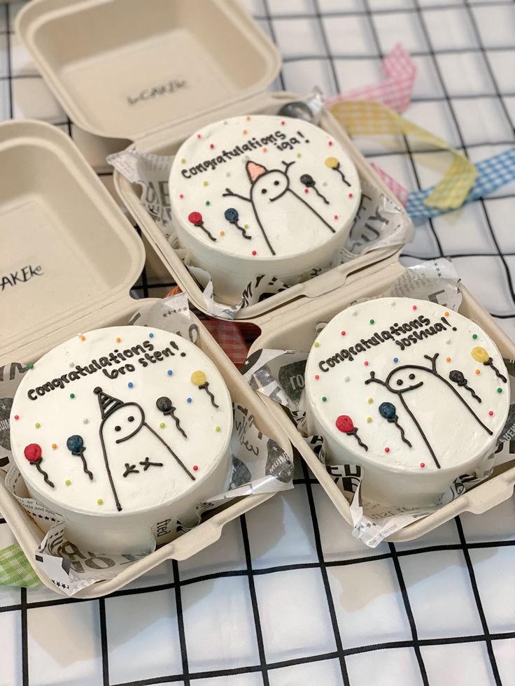 three decorated cupcakes in small boxes on a table